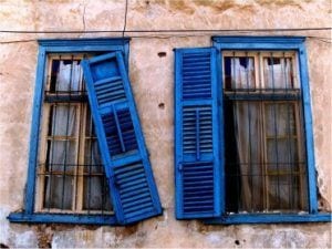שני חלונות עם תריסי עץ כחולים בקיר מתקלף
